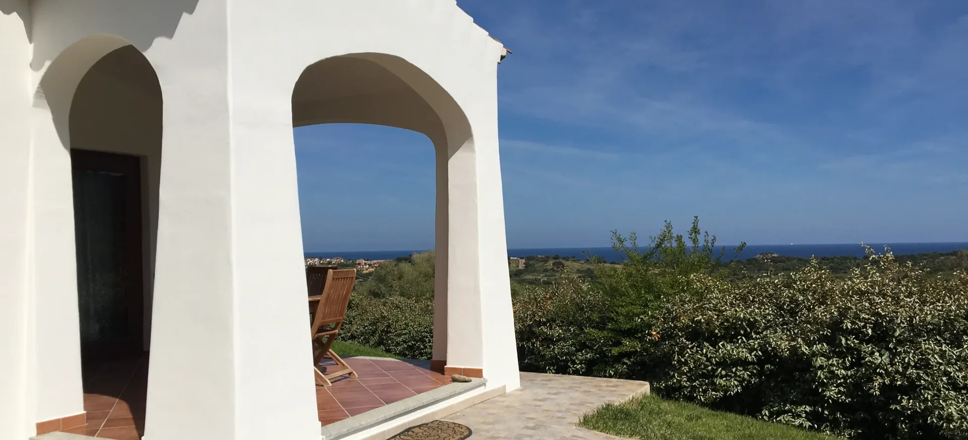 Portico bianco ad arco affacciato sul prato e sulla macchia mediterranea, con il mare all'orizzonte