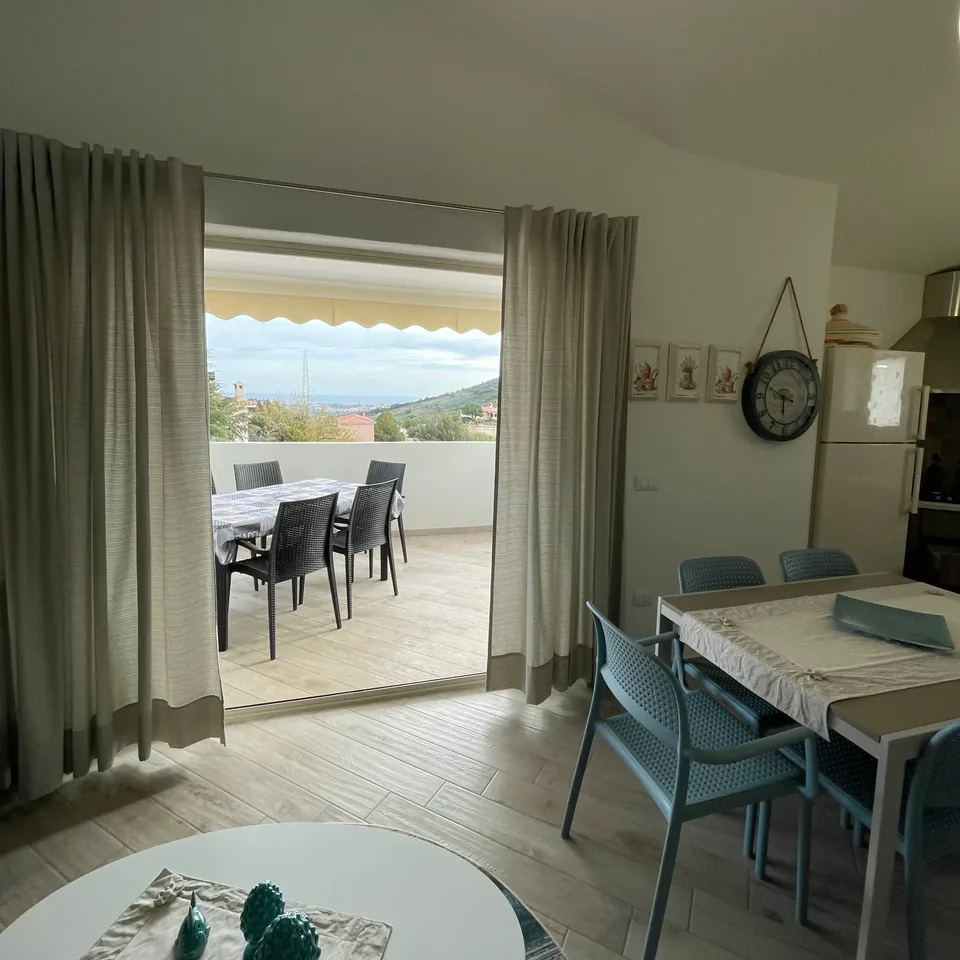 Soggiorno con tavolo e sedie azzurre che si apre su una veranda coperta